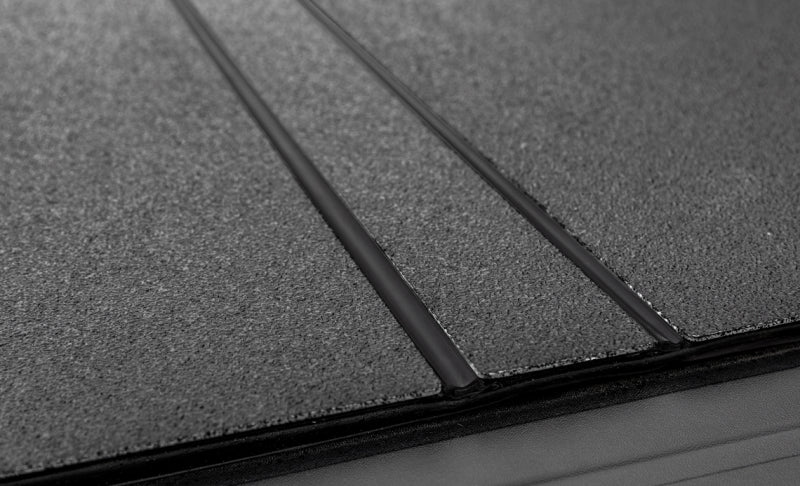 LOMAX black urethane tri-fold tonneau cover mounted on Toyota Tacoma